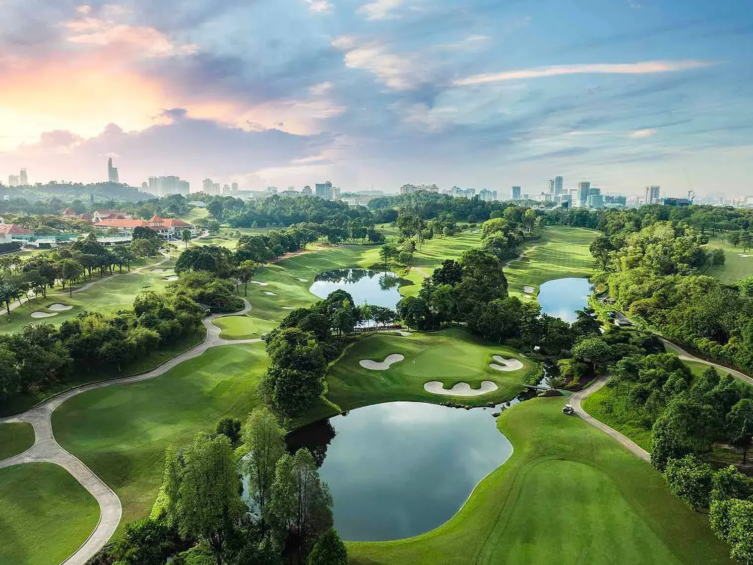 Green fairways and lakes at Bukit Jalil at sunrise, with the city beyond